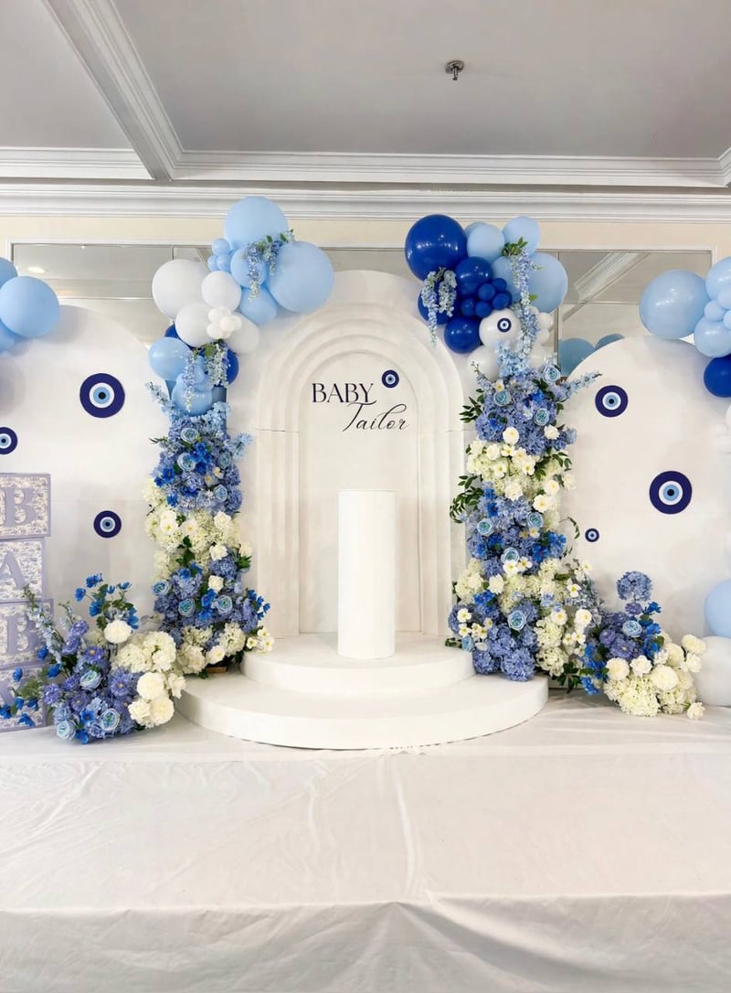 White arched backdrop with evil-eye motifs, blue balloons and blue and white florals