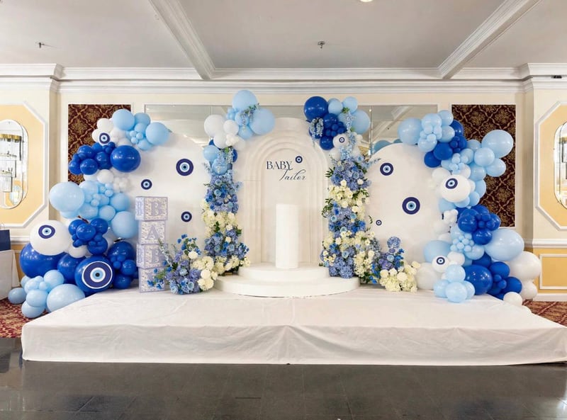Wide view of a white and blue setup with evil-eye arches, balloons and florals on a platform
