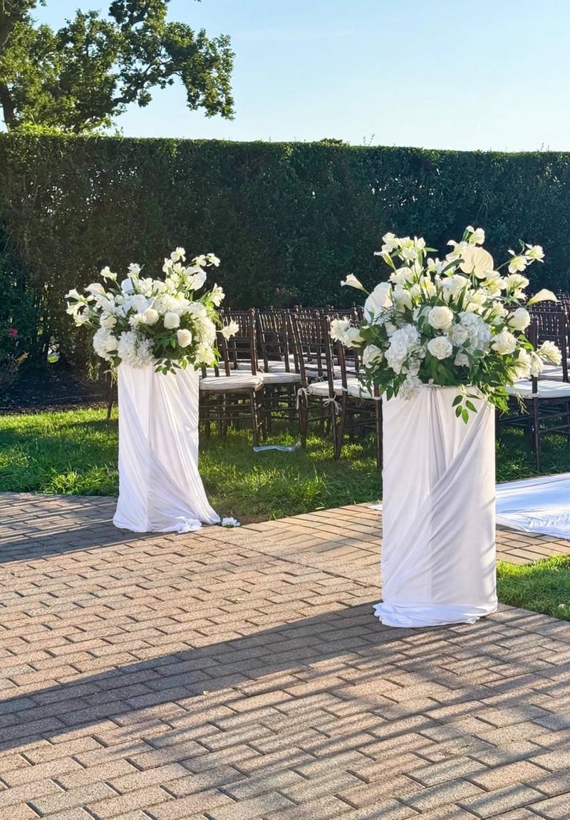 Two white draped columns topped with white floral arrangements on an outdoor patio