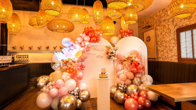Coral, peach and gold balloon arch in a restaurant under woven pendant lights