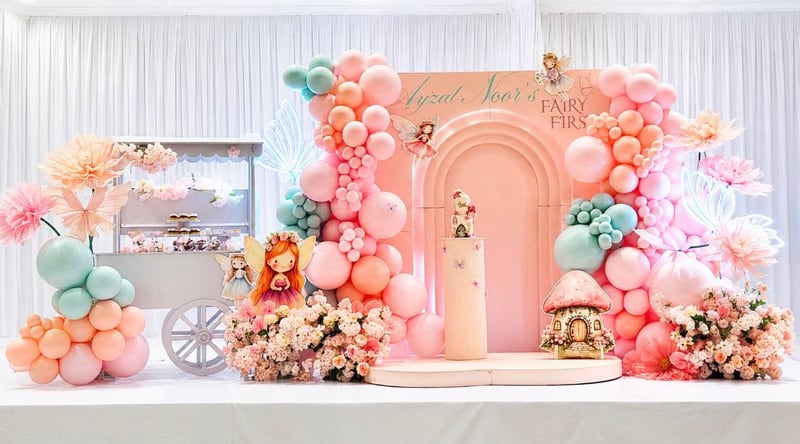 Pink and peach balloon backdrop with a mushroom house, fairy figures and a white dessert cart