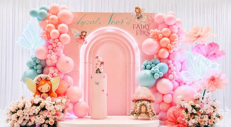 Pink arch backdrop with peach and teal balloon garlands, florals and fairy cutouts