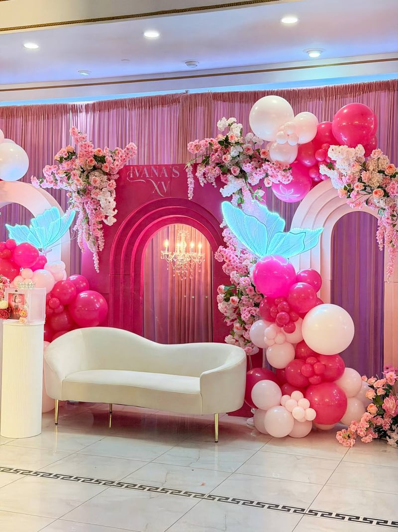 Hot pink and white balloon column with floral garlands, pink arches and a cream sofa in a ballroom