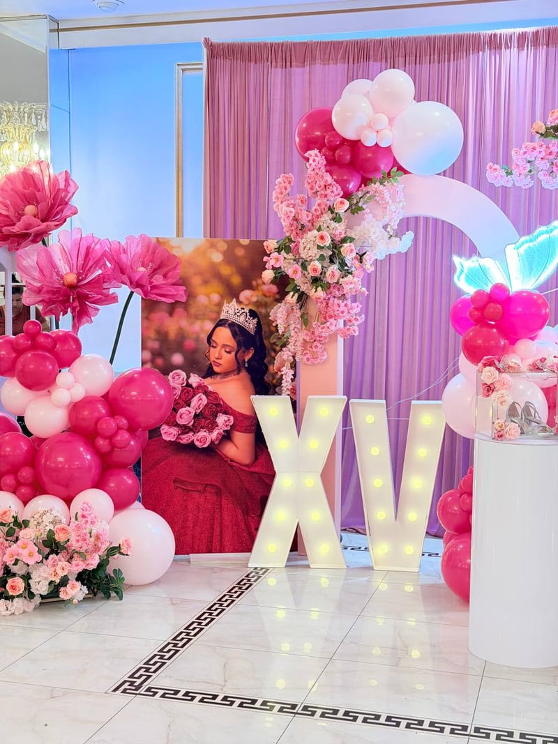 Lit XV marquee letters beside a hot pink and white balloon column, giant flowers and a framed portrait panel