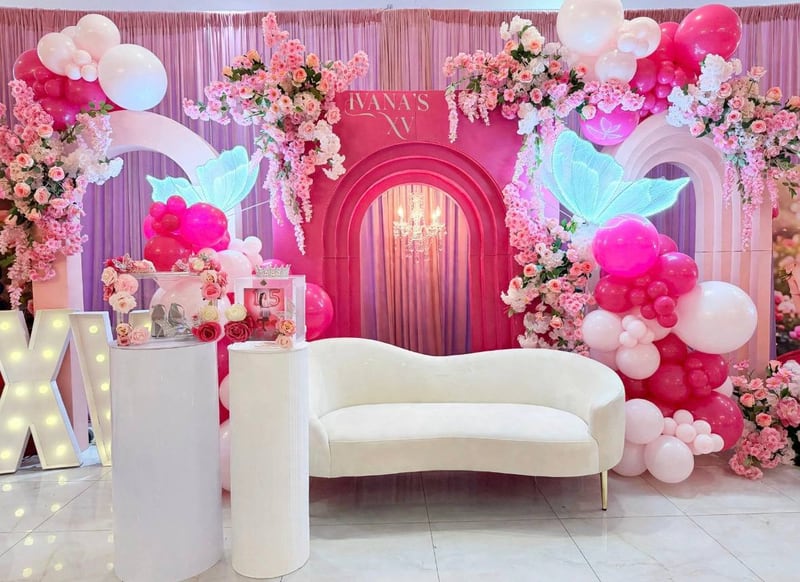 Wide view of a hot pink and white balloon, floral and arch backdrop with marquee letters and a cream sofa