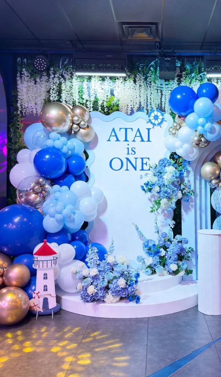 Nautical first-birthday backdrop in blue and gold balloons with white florals, seen from the side