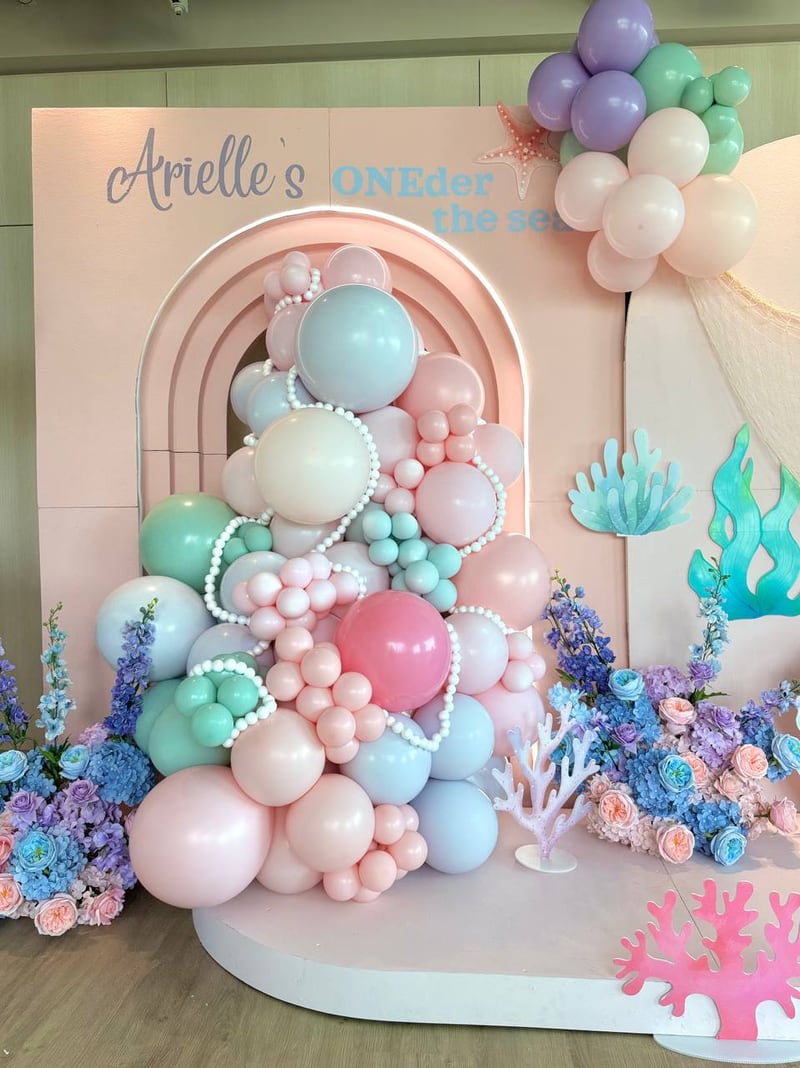 Tall pastel balloon cluster with pearl accents in front of a pink arched backdrop with a mermaid theme