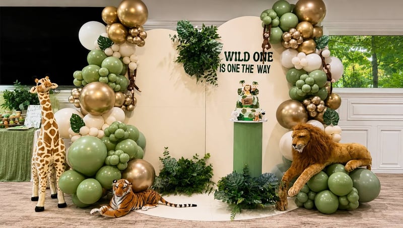 Safari-themed backdrop with sage and gold balloon garlands, greenery and plush animals