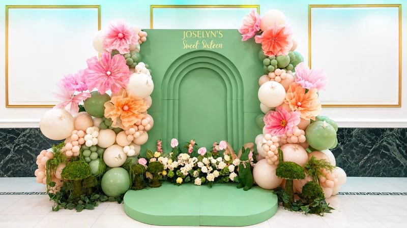 Sage green arch backdrop with pink and orange flowers, balloons and moss accents