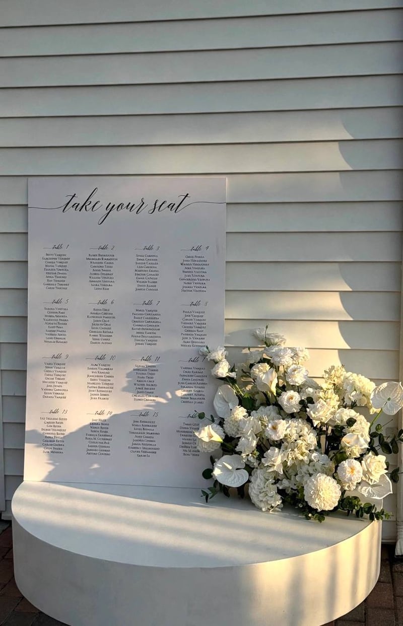 Seating chart sign on a round white plinth with a white floral arrangement