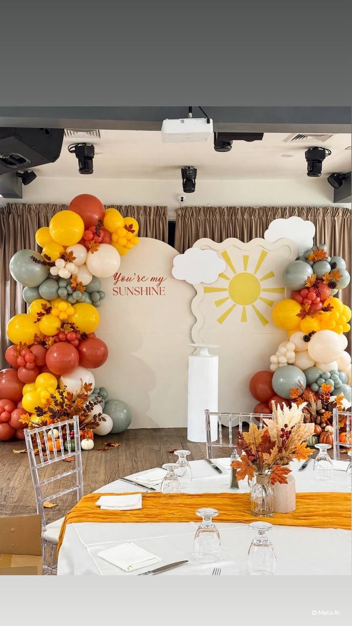 Orange, yellow and sage balloon garland around a sun-and-cloud backdrop above a styled table