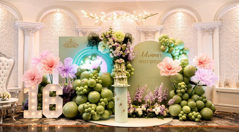 Olive and sage balloons with lit marquee numbers one and six in front of a pillared backdrop