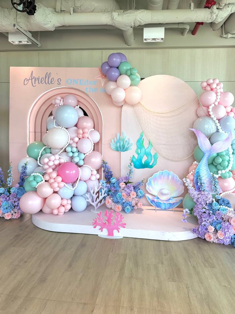 Full under-the-sea backdrop with pastel balloon garlands and seashell and mermaid-tail props on a round platform